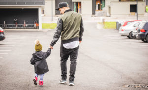 Isä ja pieni lapsi kävelevät käsi kädessä parkkipaikalla