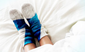 Sängyn peiton alta näkyy jalat, joissa on Suomen lipun kuvioiset villasukat