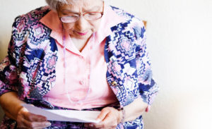 kelan kehotus hakea kansaneläkettä on tavoittanut iäkkään naisen, joka on istahtanut lukemaan kirjettä.