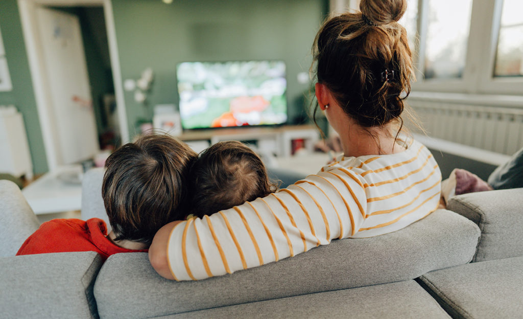 Yksinhuoltajaperheen äiti ja kaksi lasta katselevat sohvalla televisiota.