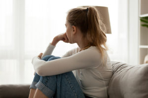 Nuori nainen istuu sohvalla ja tuijottaa ikkunasta ulos huolestuneen oloisena.