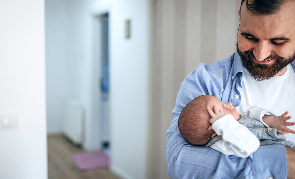 Perhevapaalla oleva mies pitää sylissään pientä vauvaa.