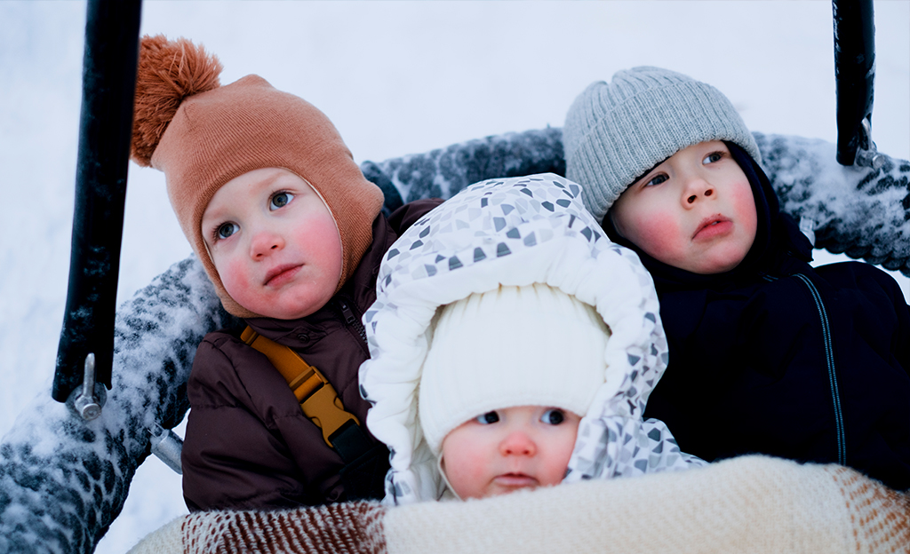 Kolme pientä lasta isossa rengaskeinussa talvitamineissaan.